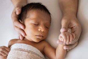 Parent Holding the Hand and Face of Sleeping Baby