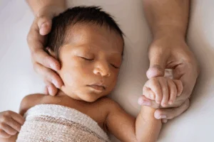 Parent Holding the Hand and Face of Sleeping Baby
