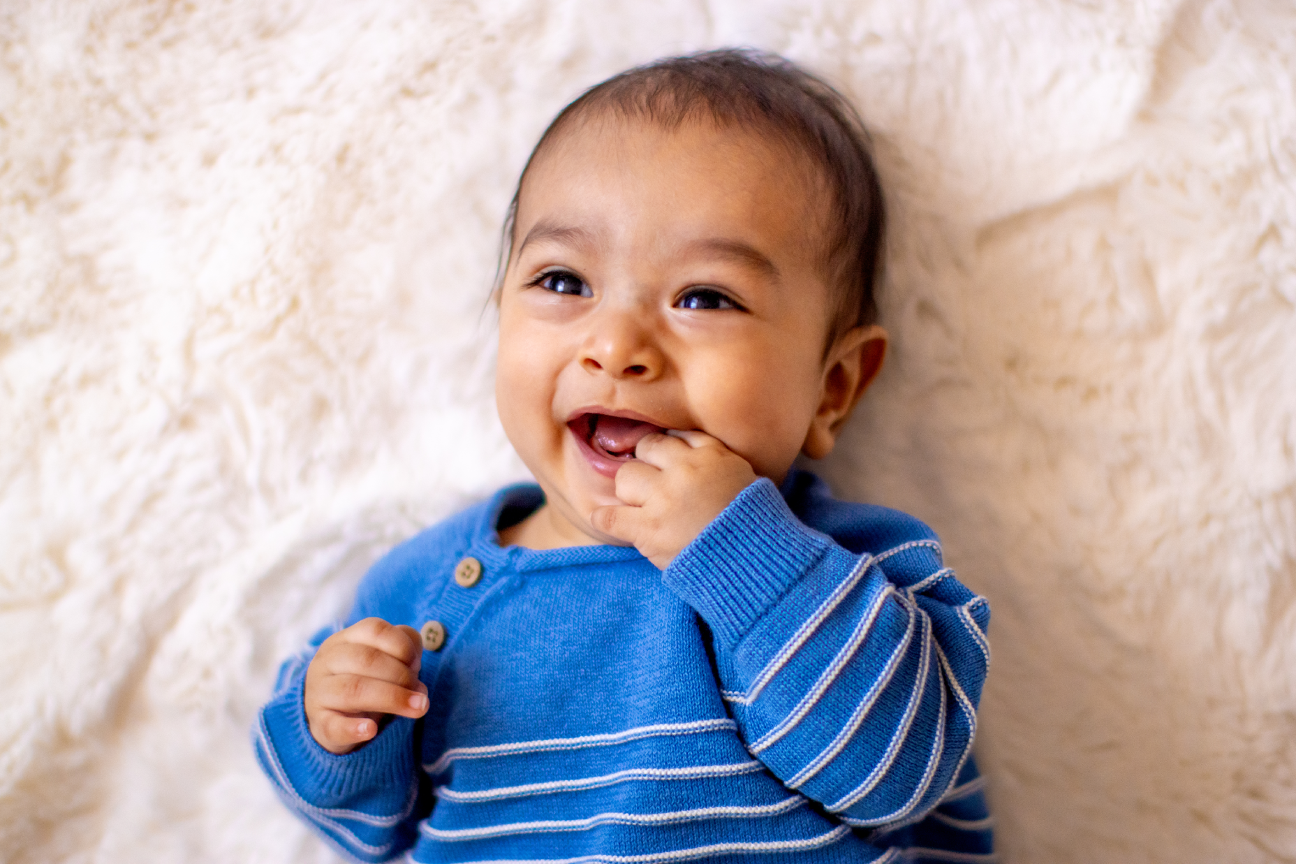 Baby in a blue outfit smiling while lying on a soft blanket