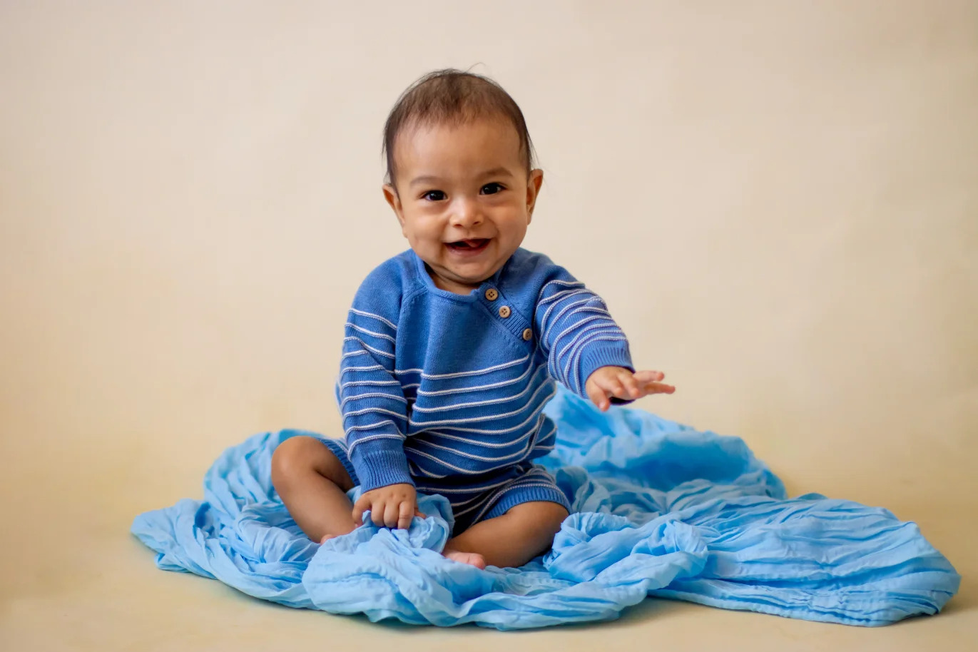 Baby in a blue outfit sitting on a blue blanket during a sitter photo session