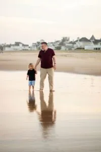 A father holding his daughter's hand near the shore during their annual family photo session