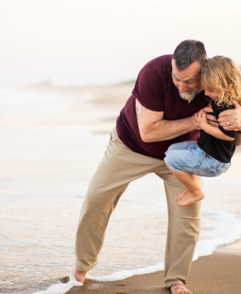 Are annual family photos worth it? A father carrying his daughter near the shore during a family photo session.