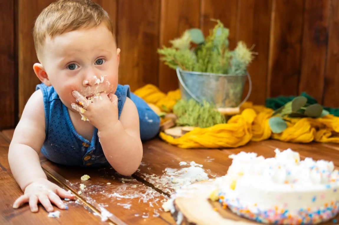 Countryside cake smash theme photoshoot showing a baby with a messy face after joyfully smashing a cake in a rustic setting.