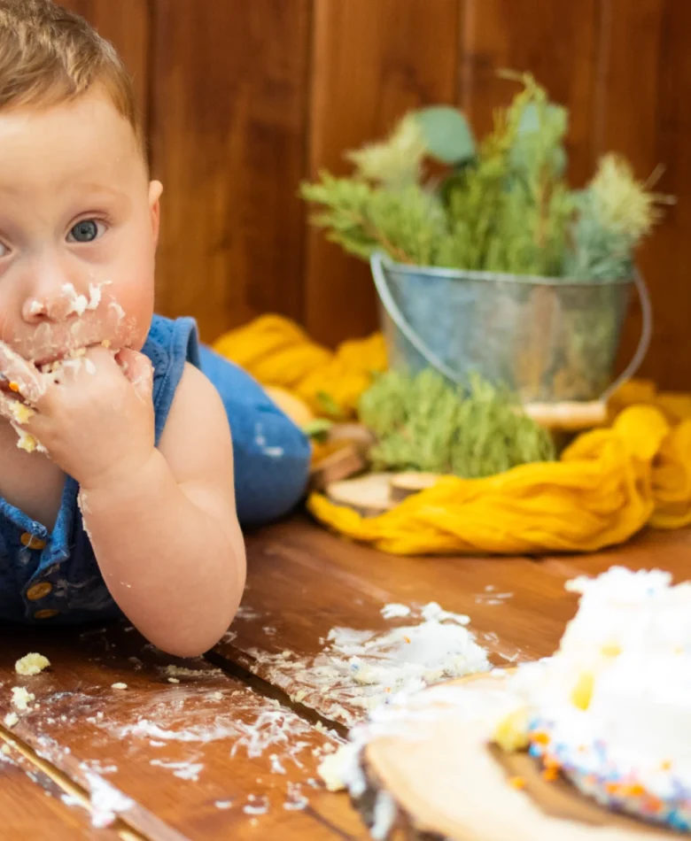 Countryside cake smash theme photoshoot showing a baby with a messy face after joyfully smashing a cake in a rustic setting.