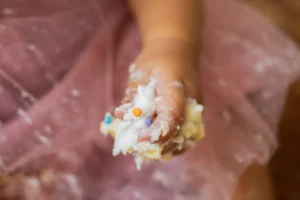 Baby holding a smashed cake in their hands during a cake smash theme photoshoot.
