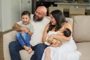 Family photo gallery moment: family of four laughing on the couch with their newborn