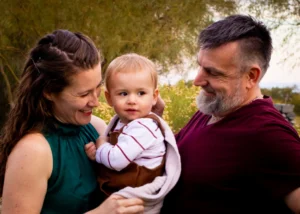 Mom and dad smiling at their toddler boy outdoors surrounded by desert greenery in the West Valley