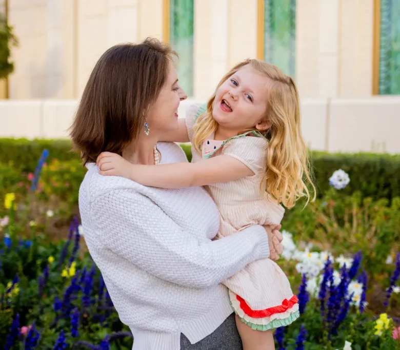 A mother lifting her laughing daughter among spring flowers during a Mother's Day family mini session in AZ.