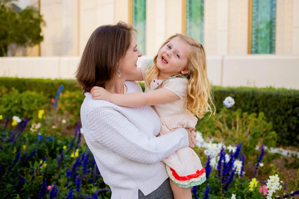 A mother lifting her laughing daughter among spring flowers during a Mother's Day family mini session in AZ.