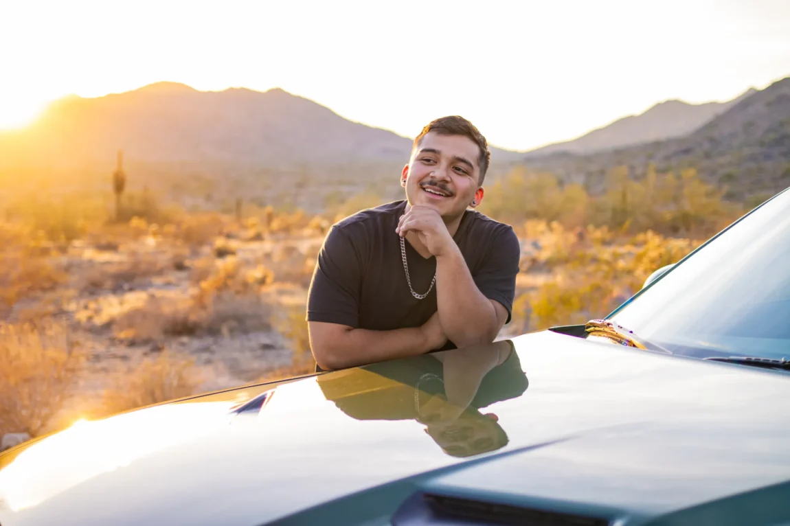 Senior guy smiling on a car hood during a golden sunset senior photo session in the Phoenix desert