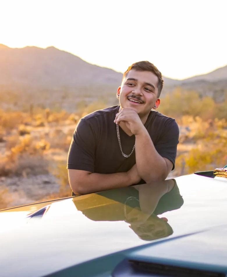 Senior guy smiling on a car hood during a golden sunset senior photo session in the Phoenix desert