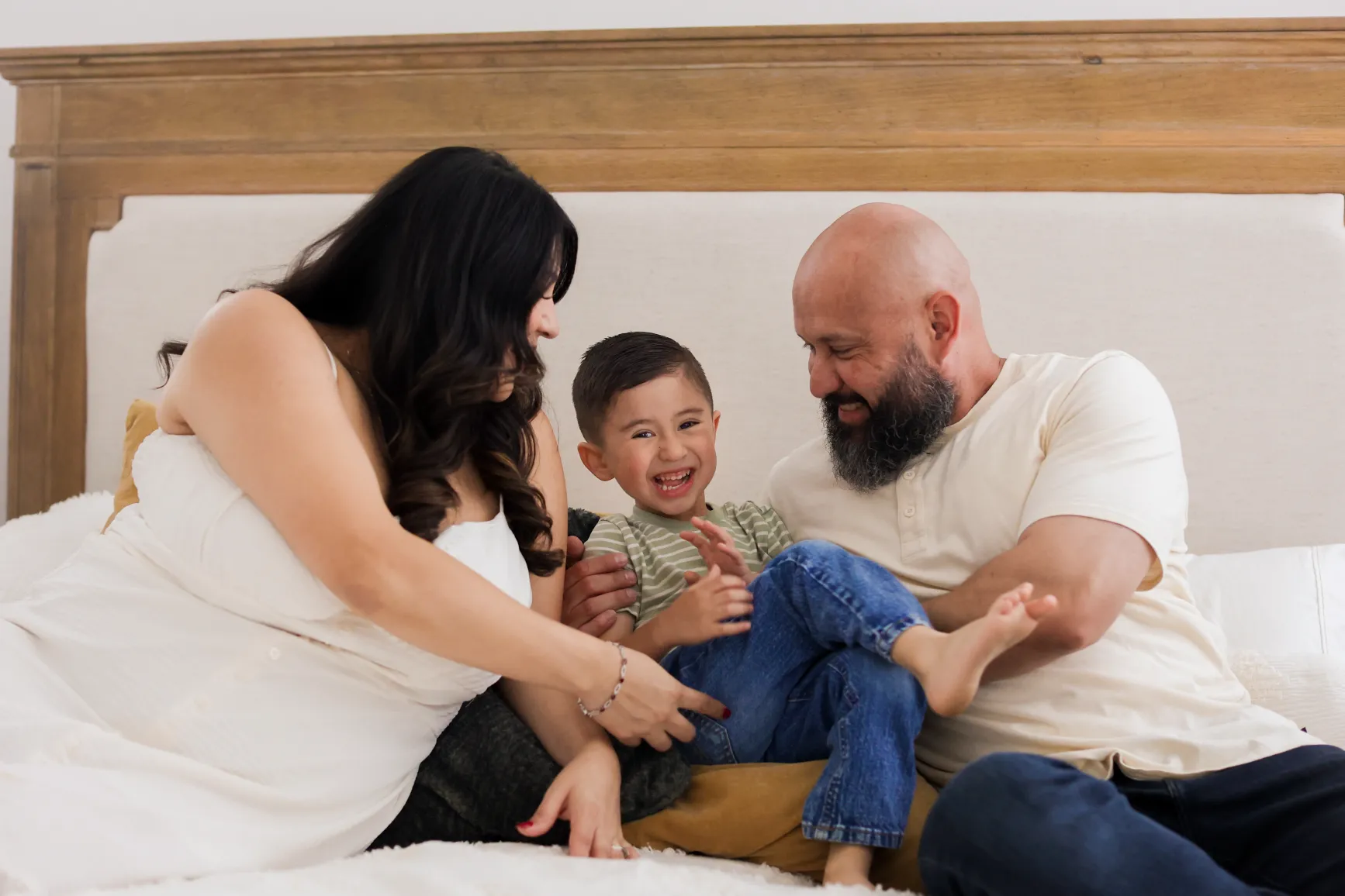 Mom and dad laughing with toddler on the bed during an in-home newborn photography session
