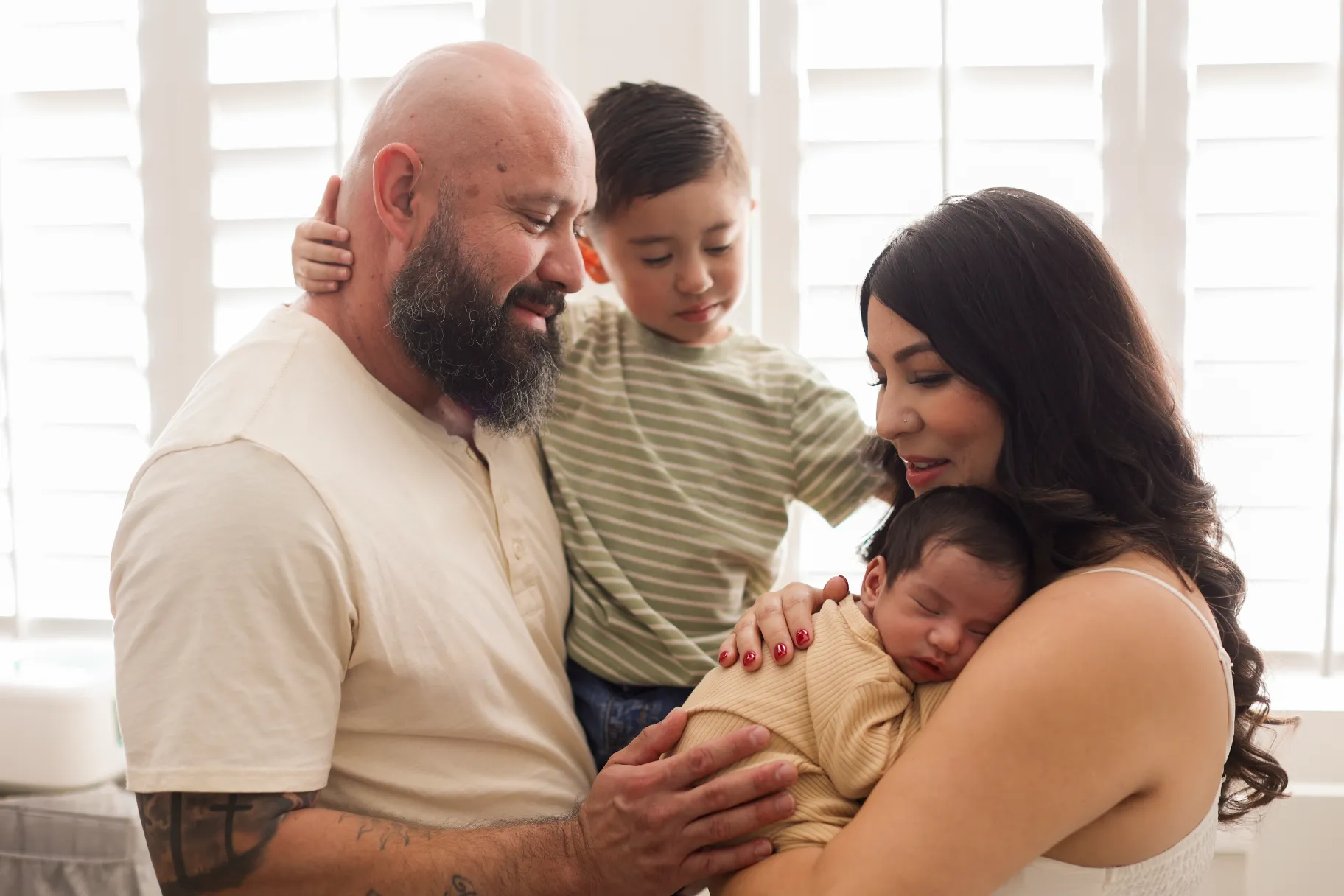 Mom and dad holding their newborn with toddler by the window during an in-home newborn photography session