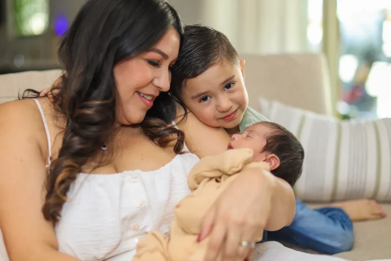 Mom sitting on the couch with her toddler and newborn during an in-home newborn photography session