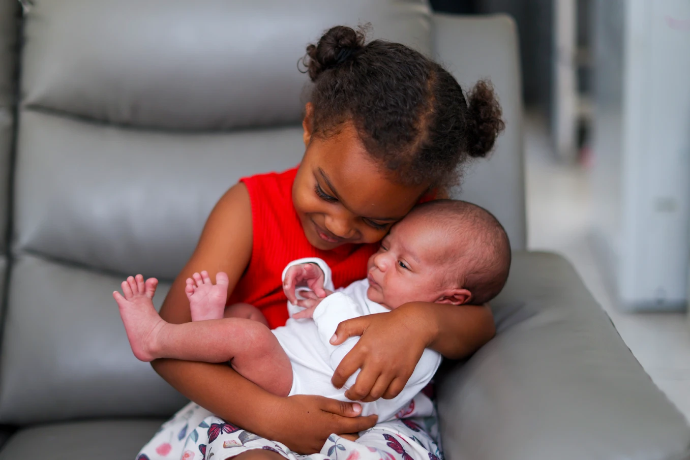Young girl smiling as she holds her newborn sibling, a precious moment that shows why newborn photos are worth it