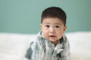 Baby boy in plaid shirt looking at camera during sitter session photography