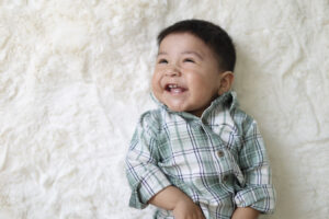 Laughing baby boy in plaid shirt on cream rug during Phoenix sitter session photography