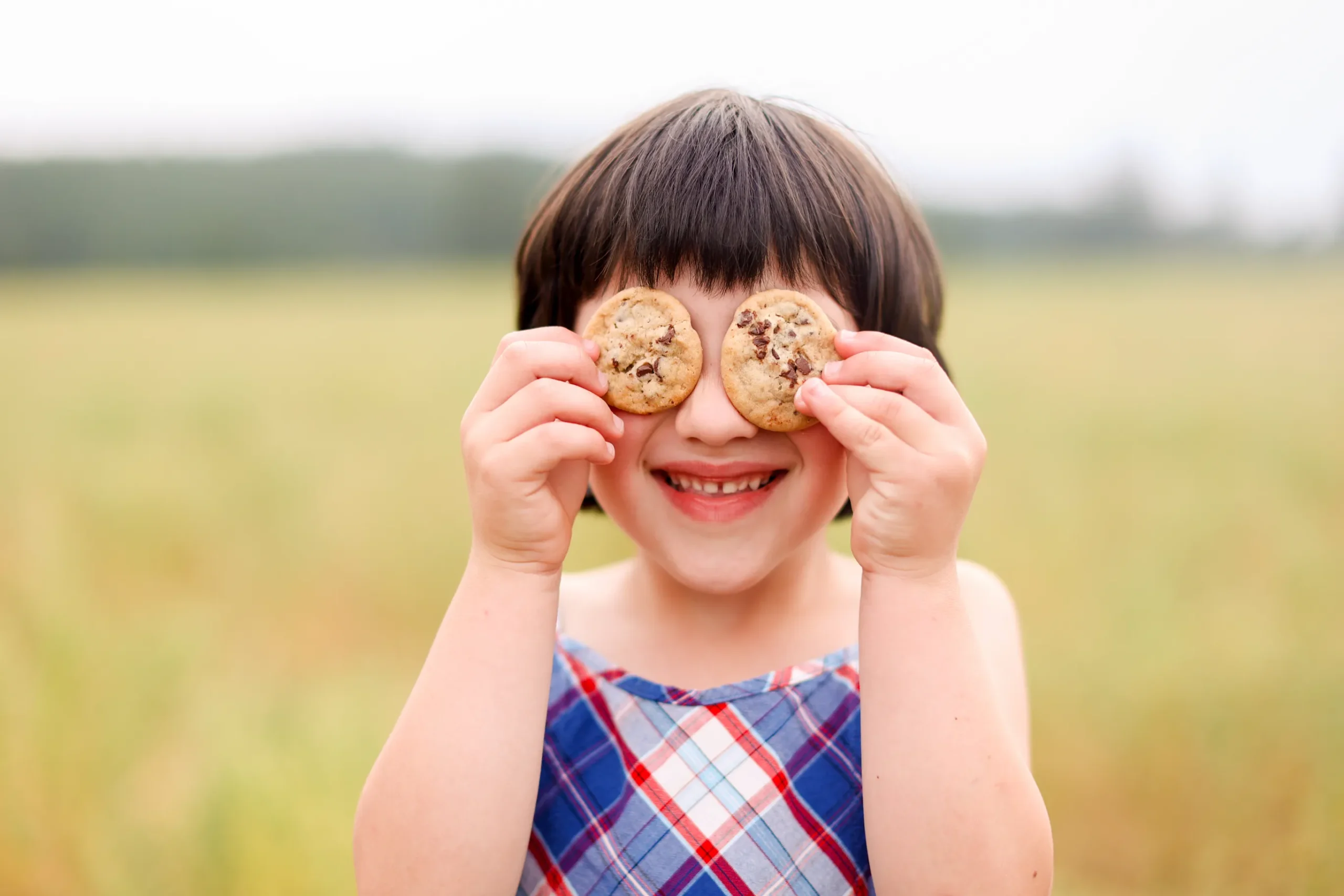 Smiling girl holding cookies over her eyes, one of the family photos to arrange family photos on a wall