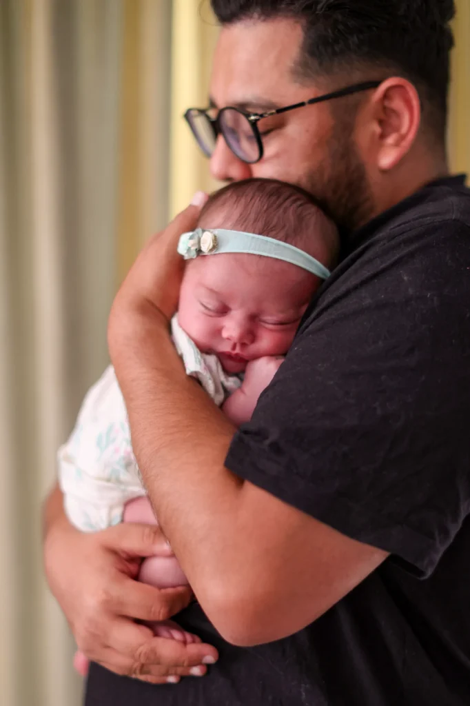 Dad cradling his sleeping newborn daughter during an in-home newborn session in Verrado
