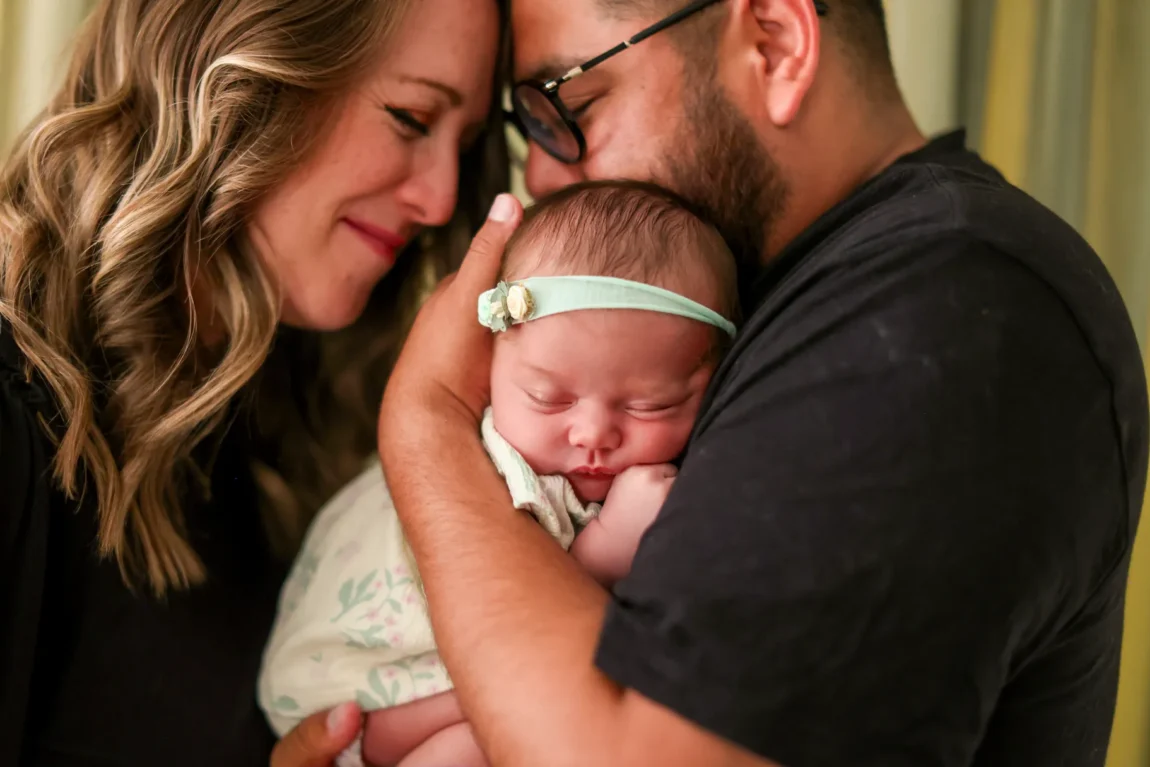 Parents leaning in close over their sleeping newborn during an in-home newborn session in Verrado
