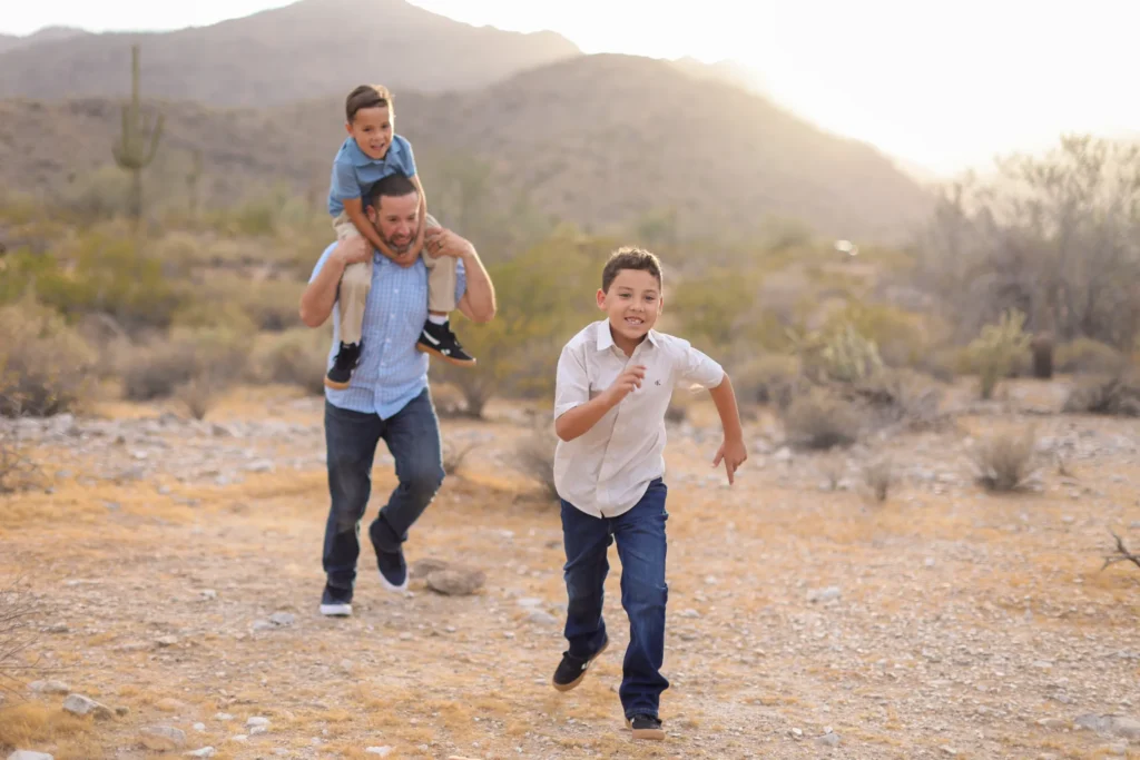 Dad and sons laughing and running through the desert during fall family photos in the West Valley