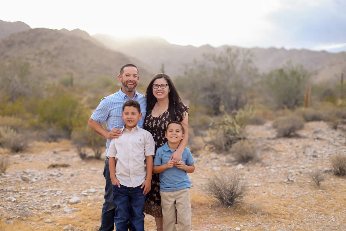 Family of four smiling together during fall family photos in the West Valley desert mountains