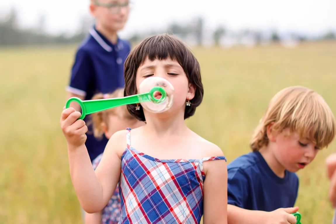 A little girl blows bubbles while her siblings wander nearby, proof that when you prepare for family photos the right way, nothing needs to be forced.