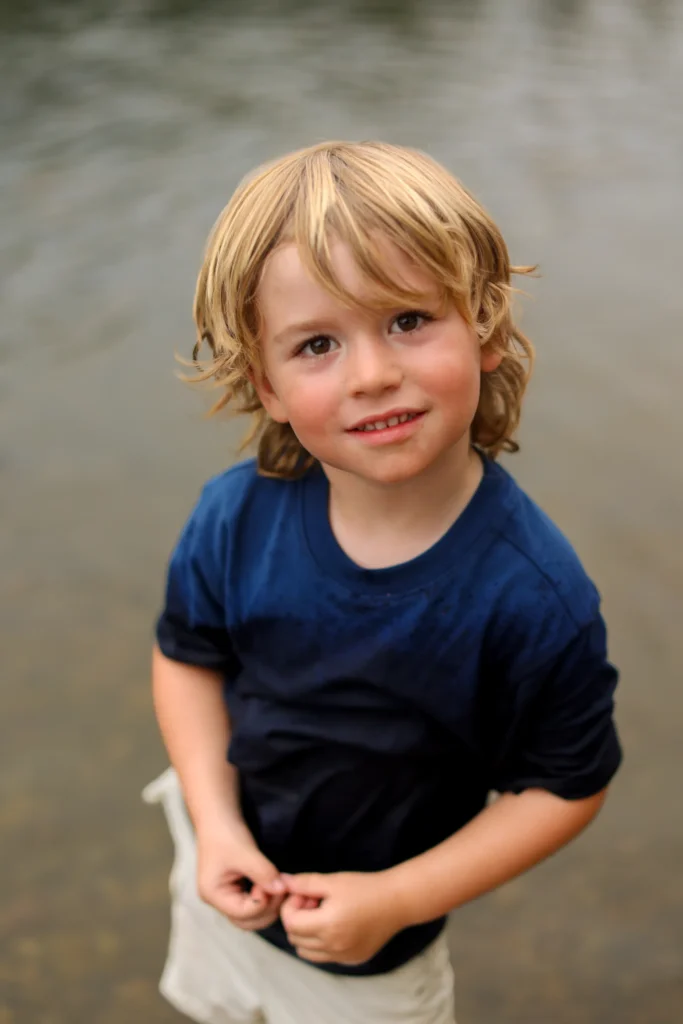Young boy with tousled hair smiling by the water during a family photo session